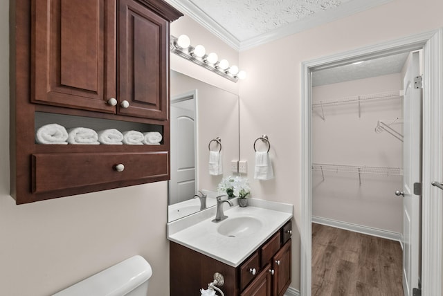 bathroom with a spacious closet, toilet, a textured ceiling, vanity, and wood finished floors