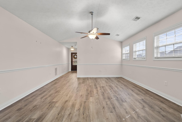 unfurnished room with a textured ceiling, lofted ceiling, wood finished floors, visible vents, and baseboards