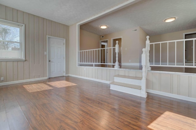 unfurnished room with a textured ceiling, wood finished floors, visible vents, baseboards, and stairs