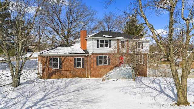 snow covered back of property featuring a chimney and brick siding