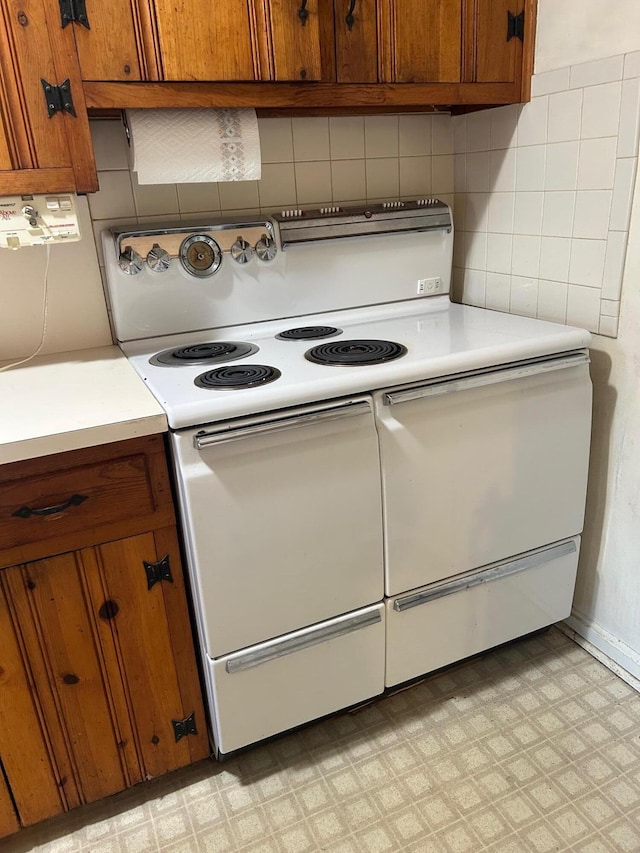 kitchen with range with two ovens, light floors, light countertops, backsplash, and brown cabinetry