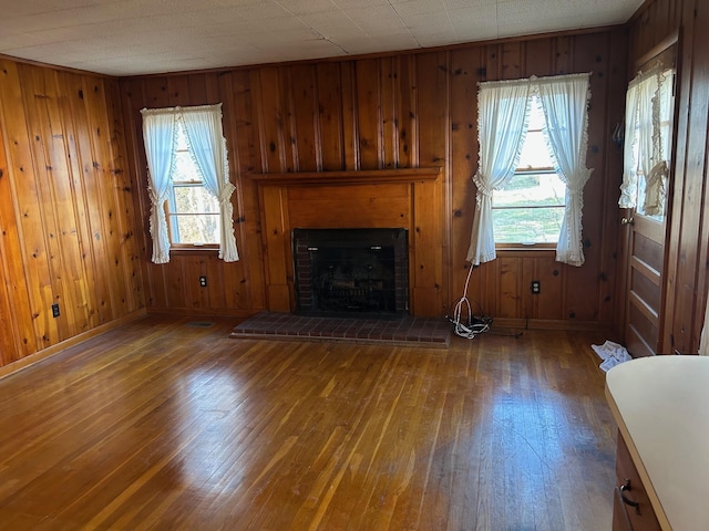 unfurnished living room with dark wood-type flooring, a brick fireplace, wood walls, and baseboards