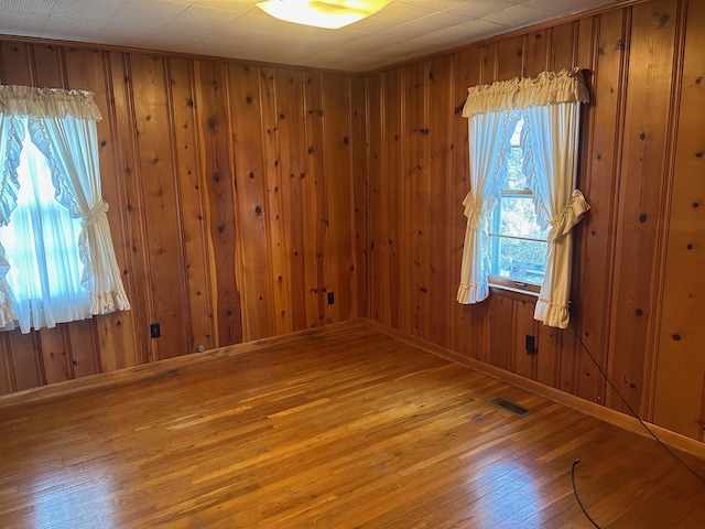 unfurnished room with baseboards, wooden walls, visible vents, and wood finished floors