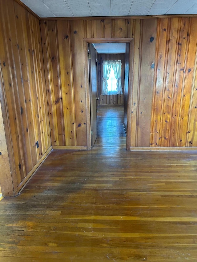 hallway featuring dark wood finished floors, wooden walls, and baseboards