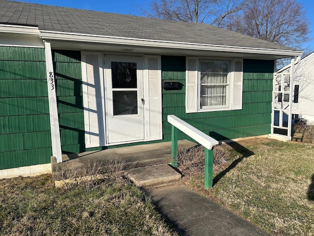 doorway to property featuring roof with shingles and a lawn