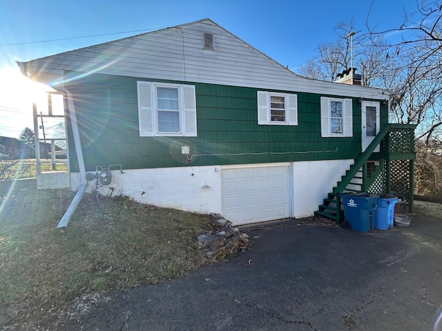 view of side of property featuring an attached garage, a chimney, stairway, and aphalt driveway