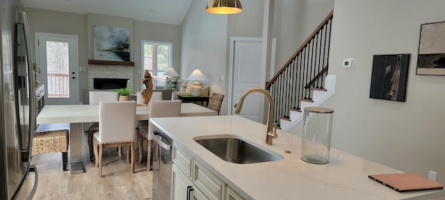 kitchen featuring lofted ceiling, sink, light wood-type flooring, stainless steel appliances, and hanging light fixtures