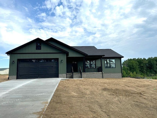 view of front of home with a garage, covered porch, concrete driveway, roof with shingles, and board and batten siding