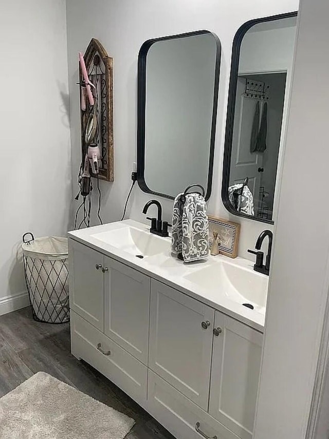 full bathroom featuring double vanity, baseboards, a sink, and wood finished floors