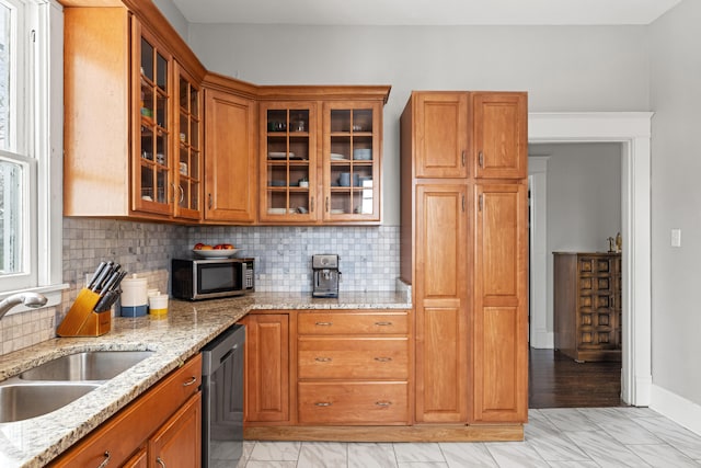 kitchen with appliances with stainless steel finishes, a sink, glass insert cabinets, and light stone countertops