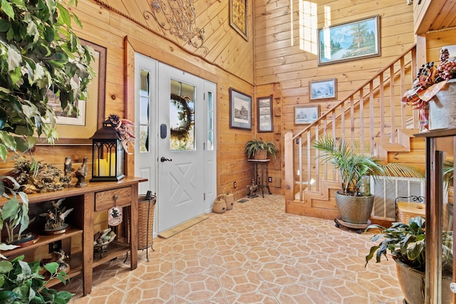 foyer entrance with wooden walls, a high ceiling, and stairs