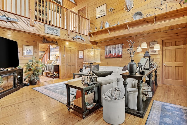 living room with a high ceiling, wood walls, stairway, hardwood / wood-style floors, and a glass covered fireplace