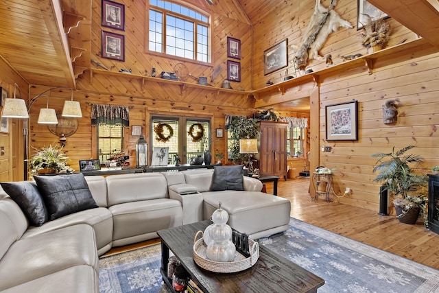 living area with wood-type flooring, a healthy amount of sunlight, wood walls, and a towering ceiling