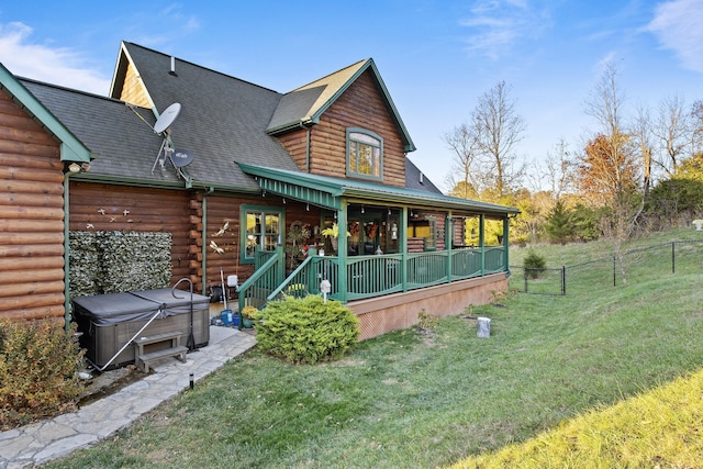 rear view of house featuring covered porch, a shingled roof, fence, a yard, and a hot tub