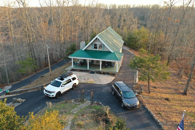 exterior space featuring a forest view, covered porch, metal roof, and aphalt driveway