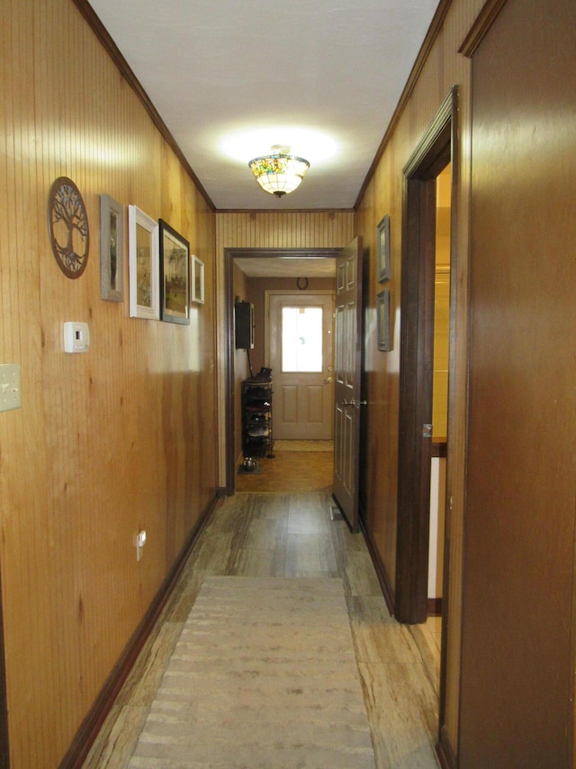 corridor with baseboards, wooden walls, and crown molding