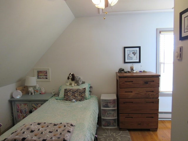 bedroom with vaulted ceiling, a baseboard heating unit, multiple windows, and light wood-type flooring