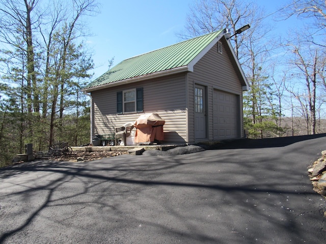 exterior space featuring a garage, metal roof, aphalt driveway, and an outbuilding