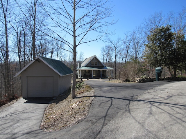 exterior space with driveway, a detached garage, metal roof, and an outbuilding