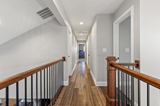 corridor featuring dark wood-style flooring, baseboards, visible vents, an upstairs landing, and attic access