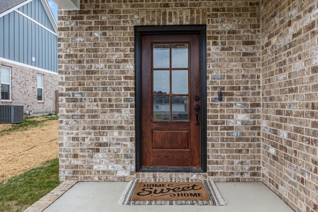 doorway to property with central AC and brick siding