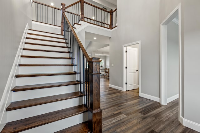 stairs featuring baseboards, a towering ceiling, and wood finished floors