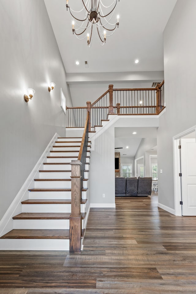 stairway featuring baseboards, wood finished floors, recessed lighting, a high ceiling, and an inviting chandelier