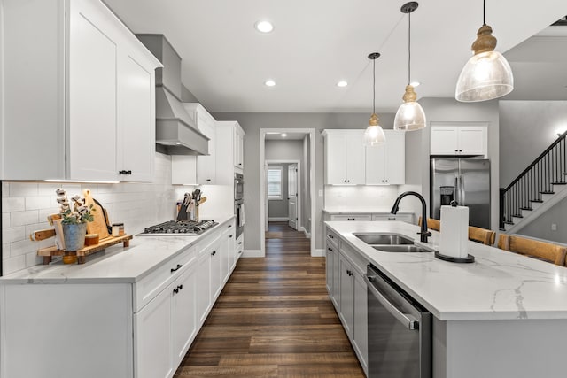 kitchen featuring premium range hood, hanging light fixtures, white cabinetry, appliances with stainless steel finishes, and a sink