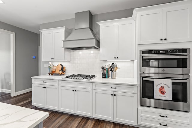 kitchen with appliances with stainless steel finishes, premium range hood, white cabinetry, and light stone counters