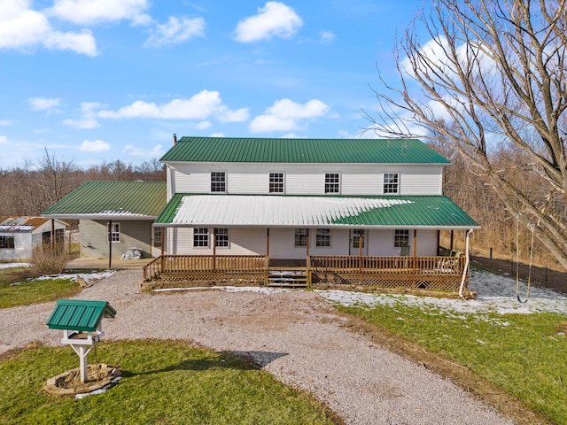 view of front facade with a front yard, gravel driveway, covered porch, and metal roof