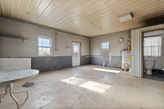 misc room featuring concrete block wall, a healthy amount of sunlight, water heater, and concrete floors