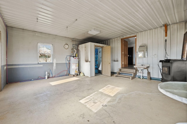 garage with concrete block wall, a wood stove, a sink, and gas water heater