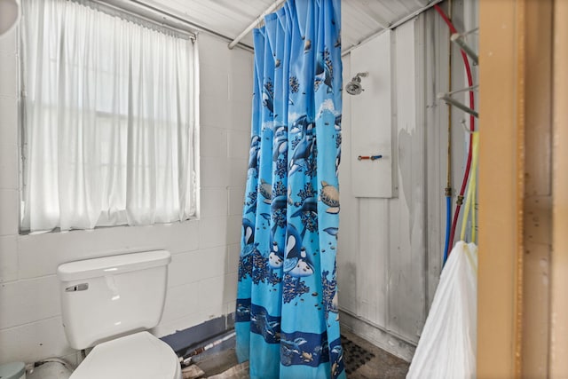 bathroom with curtained shower, concrete block wall, and toilet