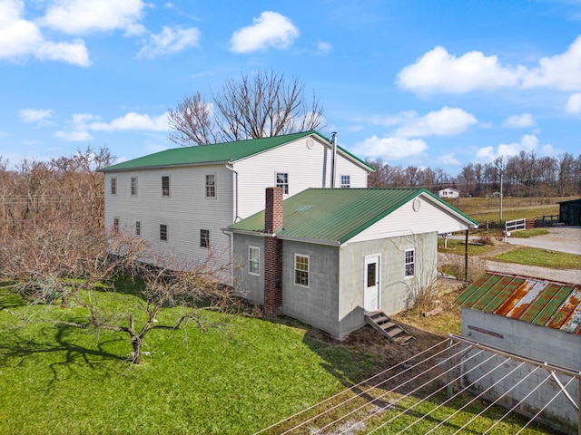 rear view of property with entry steps, a chimney, metal roof, fence, and a yard