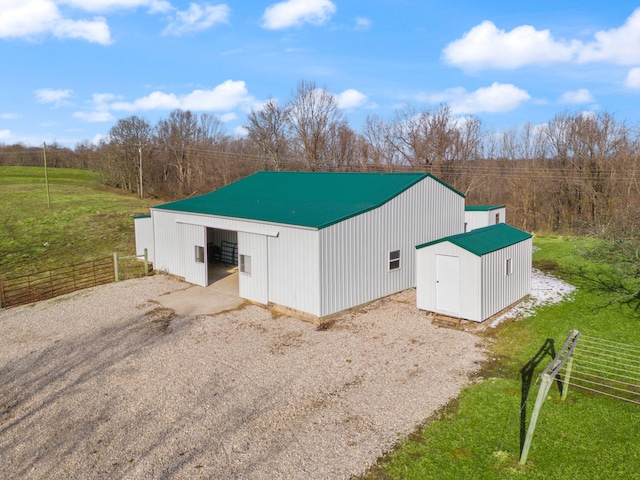 view of pole building with driveway, fence, and a yard