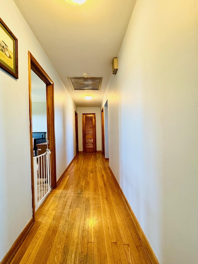 hallway with light wood-style flooring, visible vents, and baseboards