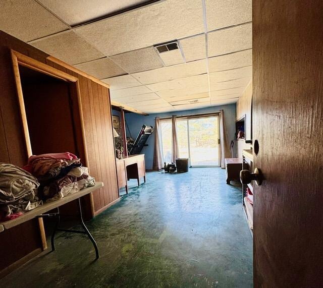 interior space with a paneled ceiling, wood walls, concrete floors, and visible vents