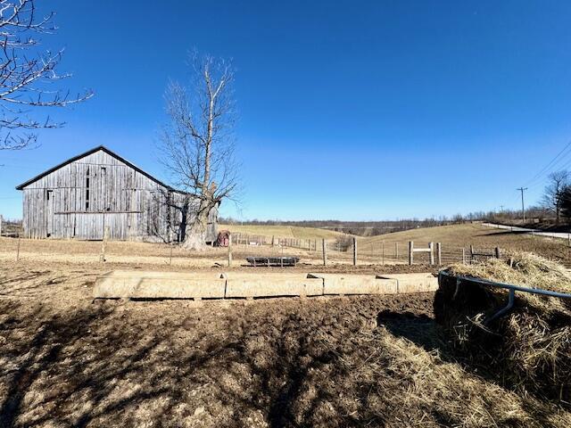 view of yard with a barn, a rural view, fence, and an outdoor structure