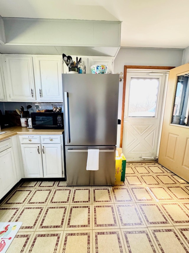 kitchen featuring freestanding refrigerator, black microwave, white cabinets, and light floors