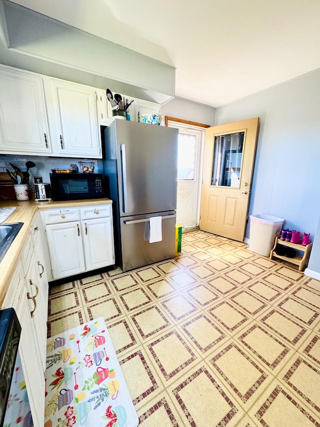 kitchen featuring black microwave, white cabinetry, light countertops, freestanding refrigerator, and light floors