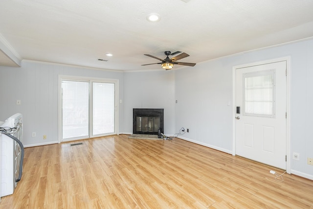 unfurnished living room with baseboards, ornamental molding, a glass covered fireplace, and light wood-style floors