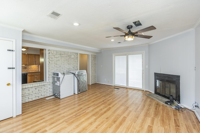 unfurnished living room with light wood-type flooring, visible vents, ornamental molding, and a glass covered fireplace