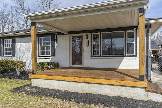 view of exterior entry featuring brick siding, fence, and a deck