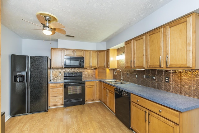 kitchen featuring dark countertops, visible vents, light wood-style flooring, a sink, and black appliances