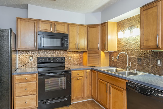 kitchen featuring black appliances, brown cabinetry, dark countertops, and a sink