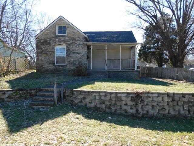 view of front of home featuring stone siding, covered porch, fence, and a front lawn