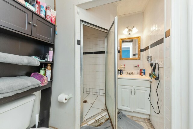 bathroom featuring tile patterned flooring, toilet, vanity, tile walls, and a tile shower