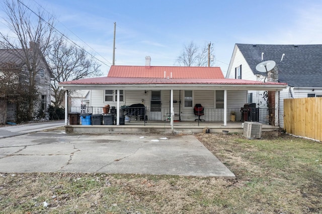 back of house featuring central air condition unit, covered porch, fence, and metal roof