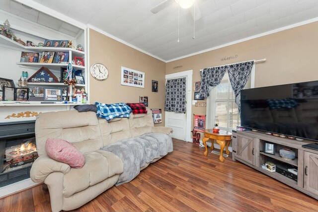 living room with a warm lit fireplace, crown molding, ceiling fan, and wood finished floors