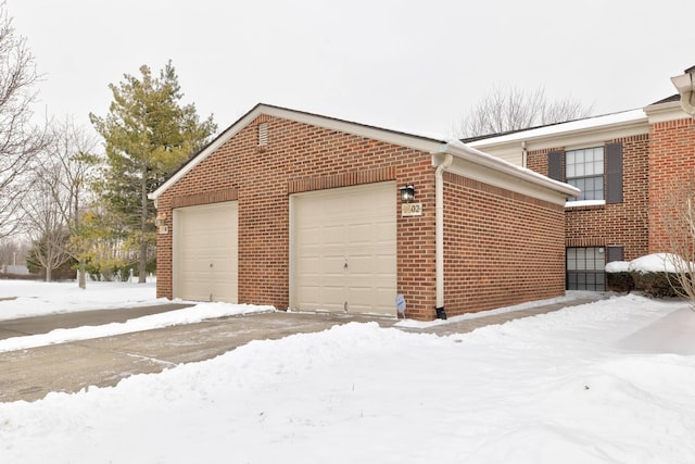 view of snow covered exterior with an attached garage, brick siding, and an outdoor structure